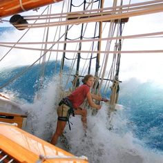 a woman climbing up the side of a sailboat in rough water on a sunny day