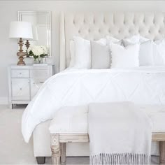 a white bed sitting in a bedroom next to a night stand and table with flowers on it