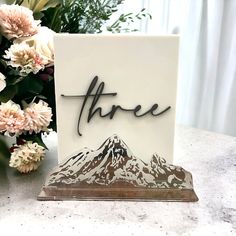 there is a card with the word three on it next to flowers and a vase