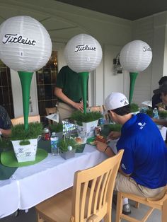 several people sitting at a table with plants and paper lanterns in the shape of golf balls