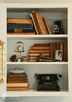 an old fashioned typewriter sitting on top of a white book shelf filled with books