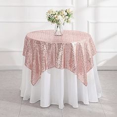 a round table with a pink and white table cloth on it, in front of a window