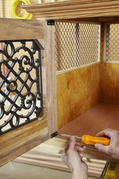 a person holding a pair of pliers in front of a wooden cabinet with iron work on it