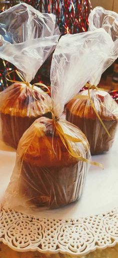 three muffins wrapped in plastic sitting on top of a doily next to a christmas tree