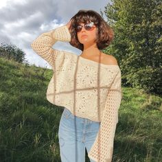 a woman standing in the grass with her hand on her head wearing sunglasses and a sweater