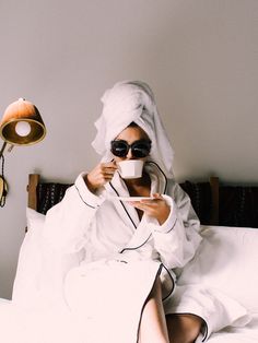 a woman sitting on top of a bed holding a cup in front of her face