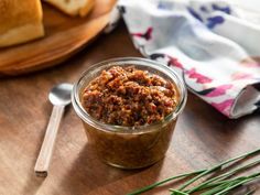 a jar filled with food sitting on top of a wooden table next to some bread