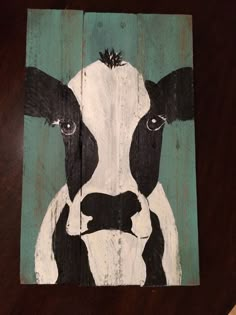 a painting of a cow is shown on a wooden board with black and white paint