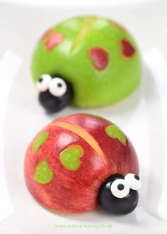 two plastic ladybugs sitting on top of each other in front of an apple