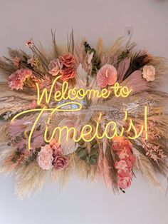 a neon sign that says welcome to timegash with flowers and feathers around it