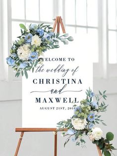 a welcome sign with blue flowers and greenery on it is displayed in front of a window