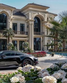 a black sports car parked in front of a large house with white flowers and palm trees