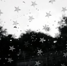 black and white photograph of stars on the window with raindrops in front of trees