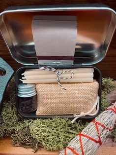 an open tin can filled with candles and other items on top of moss covered ground