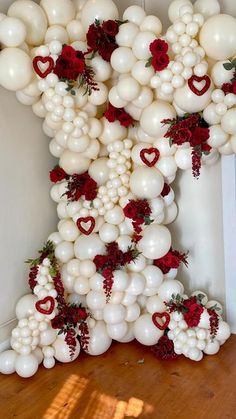 the balloon arch is decorated with red and white flowers, heart - shaped balloons, and greenery