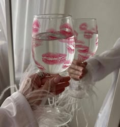 two women holding up wine glasses with pink lipstick on the rims and one is filled with water