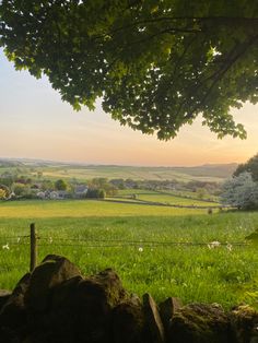 the sun is setting over an open field with rocks and trees in the foreground