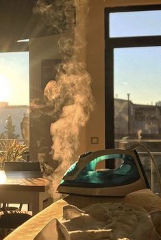 steam rising from an iron on top of a bed in front of two large windows