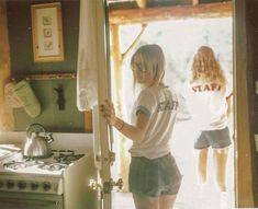 a woman standing in front of a stove top oven next to a kitchen counter with a towel hanging from it's door