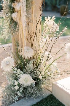 a vase filled with white flowers sitting on top of a grass covered ground next to a wooden post