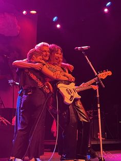 two people hugging each other on stage with microphones in front of them and purple lighting behind them