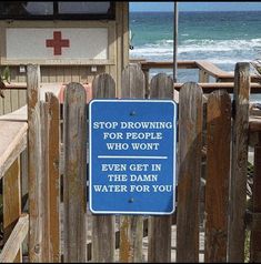 a blue sign that is on the side of a wooden fence near the ocean and beach