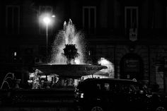 a black and white photo of a fountain at night