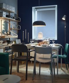 a dining room with blue walls and wooden flooring is lit by a large window