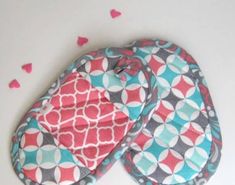 two oven mitts sitting on top of a white table covered in pink and blue hearts