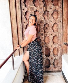 a woman leaning against a wooden door with her leg on the railing and smiling at the camera