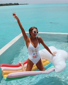 a woman in a white bathing suit holding a wine glass while standing on an inflatable raft