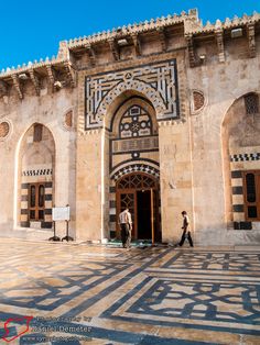 two men walking in front of a building with intricate designs on the walls and doors