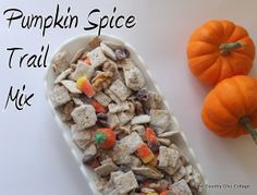 a white bowl filled with candy corn and pumpkin spice treats next to two small orange pumpkins