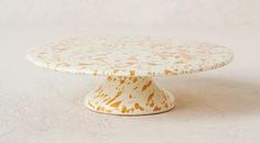 a white cake plate with yellow flowers on it sitting on a tablecloth covered surface