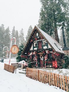 a small house covered in snow next to a wooden fence and christmas decorations on the outside