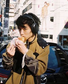 a young man wearing headphones and eating a doughnut on the street in front of a car