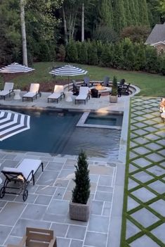 an outdoor swimming pool with lounge chairs and umbrellas next to it, surrounded by greenery