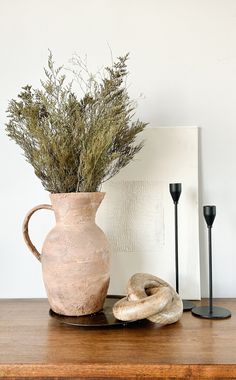 a vase with some plants in it sitting on a table next to two black candles