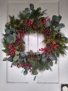 a wreath on the front door with berries, holly and pine cones hanging from it