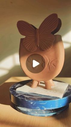 a clay bird sculpture sitting on top of a wooden table next to a blue bowl