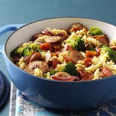 pasta with sausage, broccoli and tomatoes in a blue pot on a table