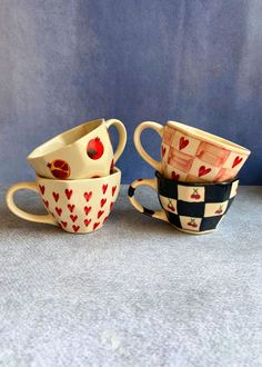 three cups with hearts painted on them sitting side by side in front of a blue wall