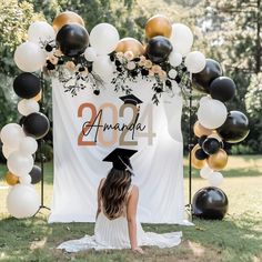 a woman sitting on the ground in front of a graduation arch with balloons and flowers