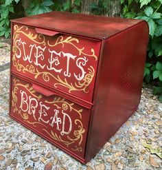 a red and gold painted wooden box sitting on top of gravel next to some trees