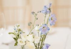 two vases filled with flowers on top of a white table cloth covered dining room table