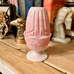 a pink glass vase sitting on top of a wooden table next to bookshelves