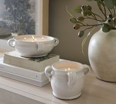 two white bowls on top of each other next to a vase with candles in it