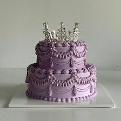 a three tiered cake with purple frosting and silver decorations on top, sitting on a white surface