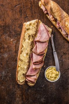 a ham and cheese sandwich on a wooden table next to a bowl of mayonnaise