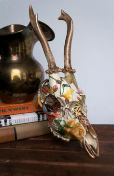 a gold vase and some books on a wooden table next to a deer's head